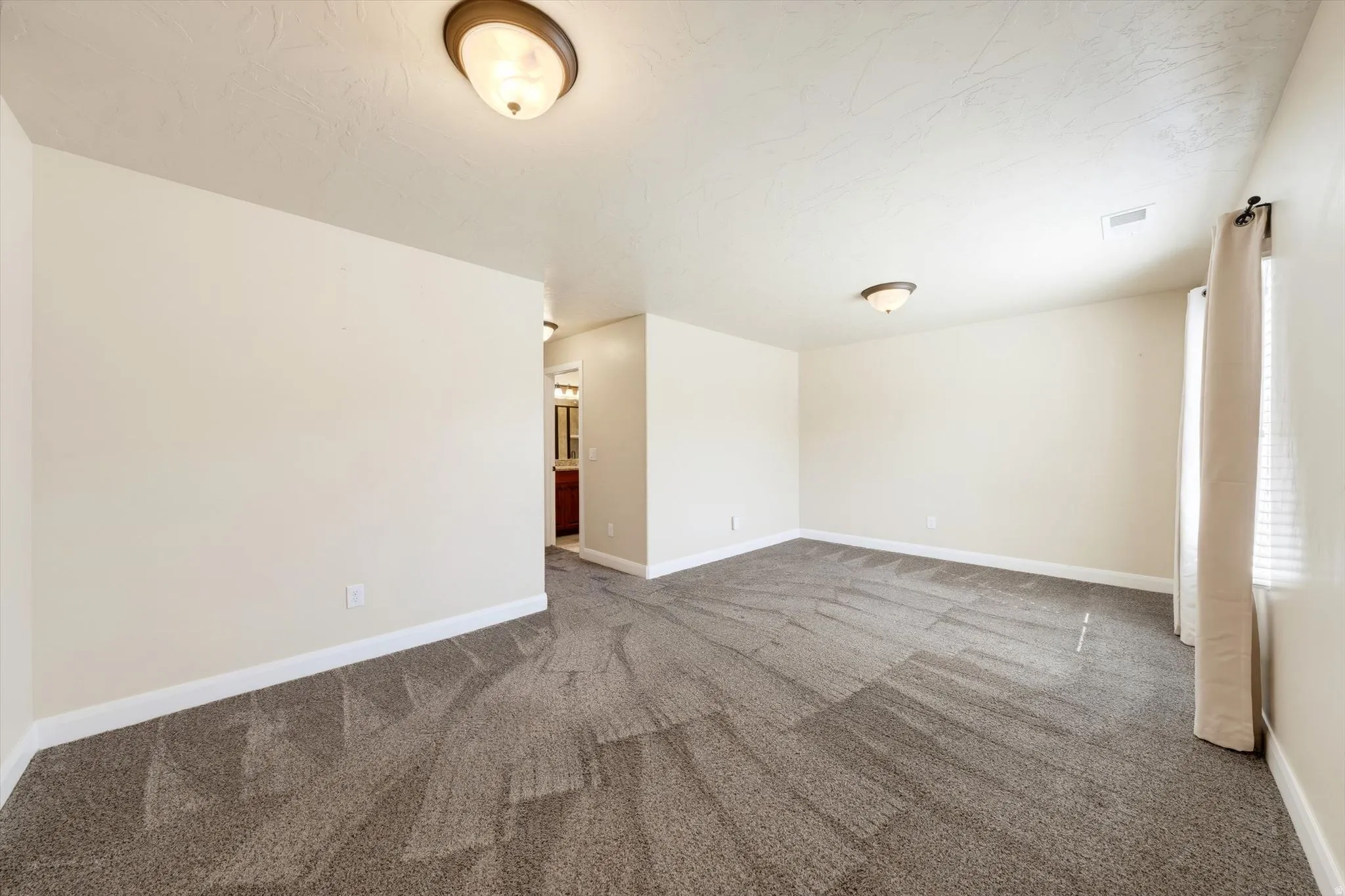 Spacious room with neutral wall tones and textured carpet flooring