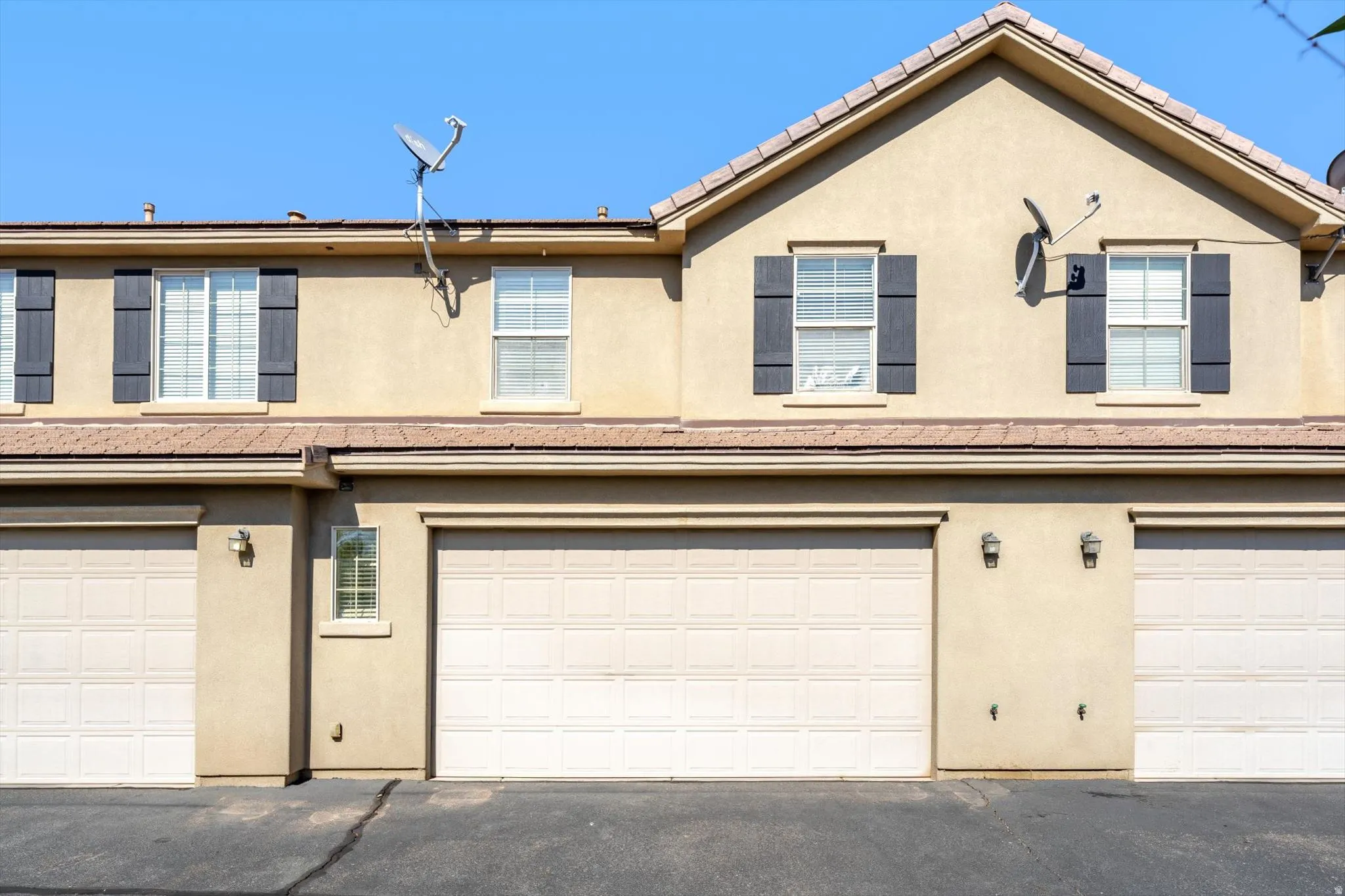 Stucco exterior with multiple garage bays, individual windows with contrasting shutters, and a pitched tile roof