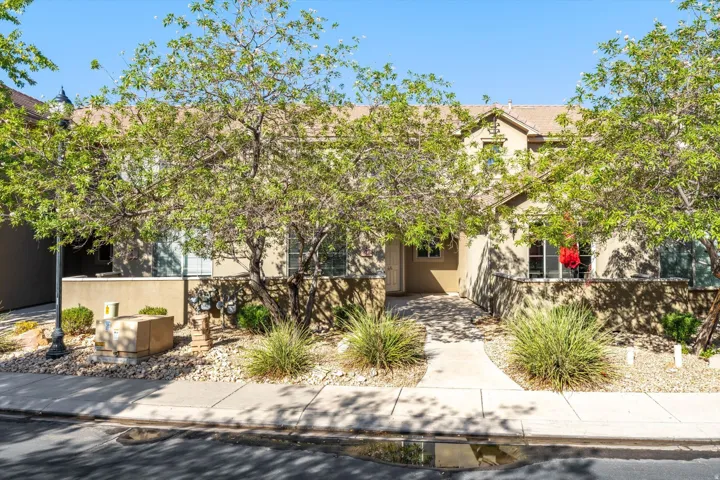 Stucco exterior with a tiled roof, featuring a concrete pathway, landscaped rock beds, and mature trees