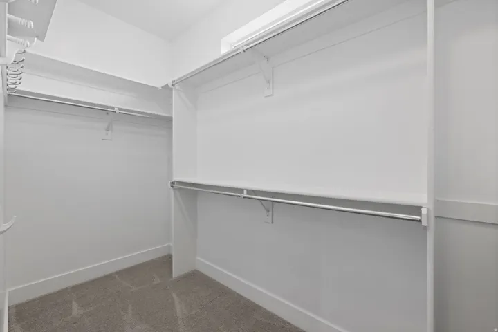 Walk-in closet featuring white built-in shelving, chrome hanging rods, and carpet flooring