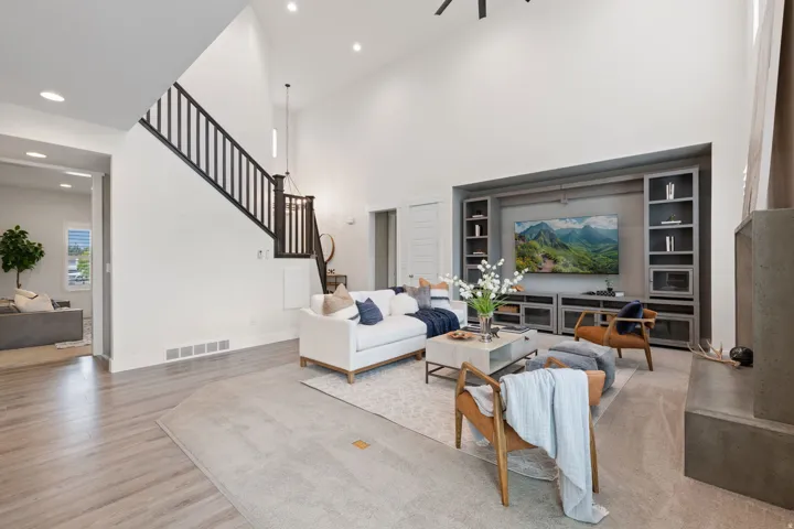 Vaulted ceilings with recessed lighting, wood-finish flooring, staircase with dark wood handrail and balusters, built-in entertainment center with shelving, and a concrete-finish fireplace surround