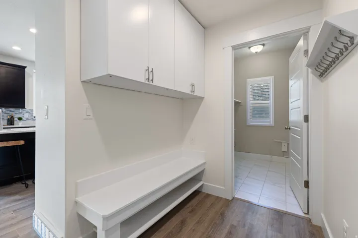 Built-in bench with storage, overhead white cabinetry, and wood-finish flooring