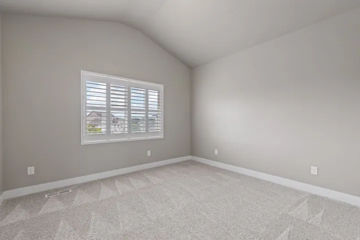 Bright, light-filled bedroom showcasing neutral wall finishes, plantation shutter window treatments with multiple panes, and plush carpeting throughout