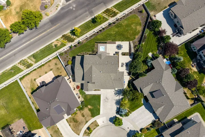 Asphalt shingle roof, paved driveway, concrete patio, built-in hot tub, and surrounding green lawn