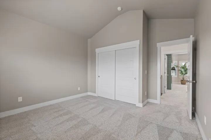 Vaulted ceiling, neutral wall paint, light-toned carpet, white trim throughout, and sliding closet doors