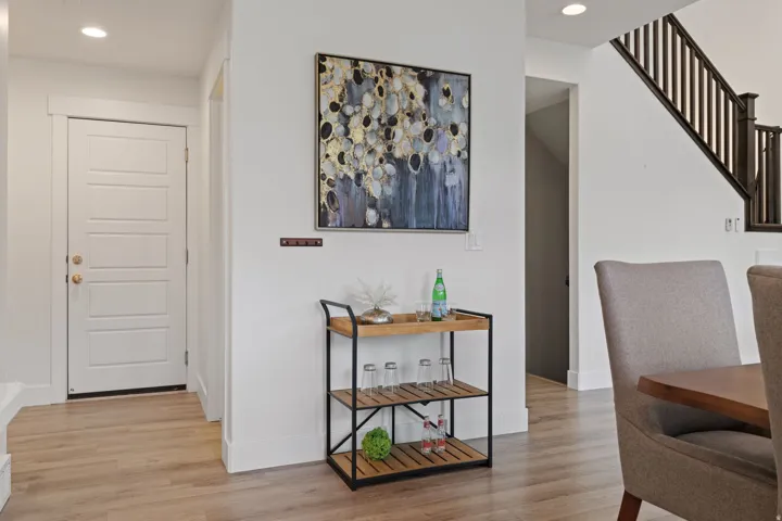 White paneled door with gold-finish hardware, light wood-finish flooring, recessed ceiling lighting, and dark wood stair railings, door leading to the garage and the stairs to the basement level.