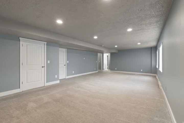 Spacious room featuring neutral carpeting, recessed ceiling lighting, light blue wall paint, white trim, and two white panel doors