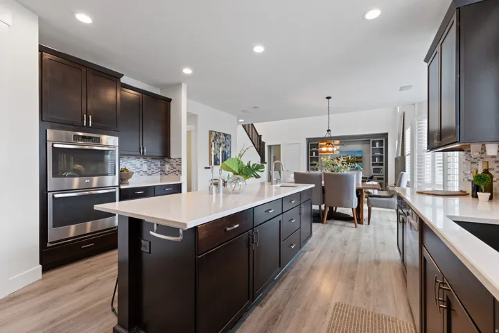 Kitchen featuring dark wood cabinetry, light countertops, stainless steel built-in oven, and wood-finish flooring