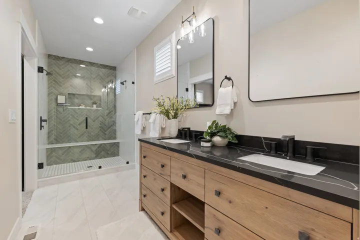 Dual vanity with dark countertops and integrated sinks, wood-finish cabinetry, and matte black fixtures