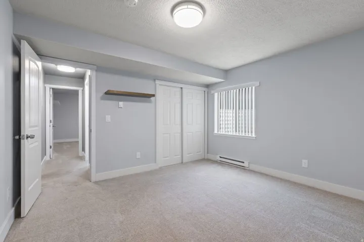 Carpeted room featuring a window with vertical blinds, a built-in shelf, and a sliding closet door