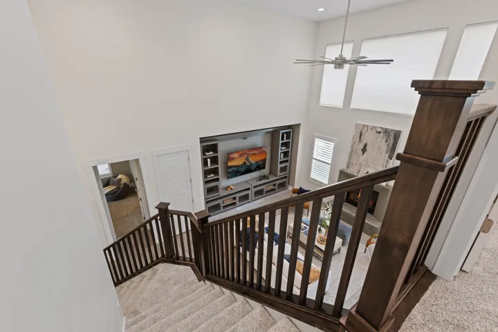 Two-story living area with a ceiling fan, a built-in media center, a fireplace, and multiple windows
