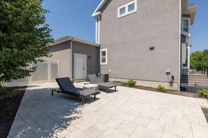 Paved patio area, stucco exterior, white privacy fence, exterior door, and wooden deck with railing