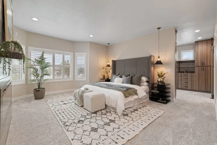 Recessed lighting, bay windows with plantation shutters, plush carpeting, a built-in upholstered headboard, and integrated closet storage