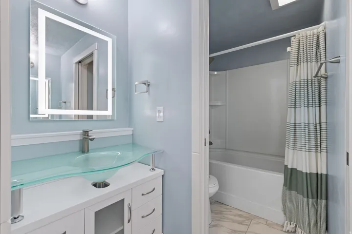 White vanity with clear glass vessel sink and brushed nickel faucet