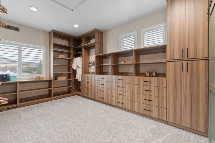 Built-in wood-finish cabinetry, integrated shelving, multiple drawers with dark hardware, two windows with louvered blinds, and recessed lighting