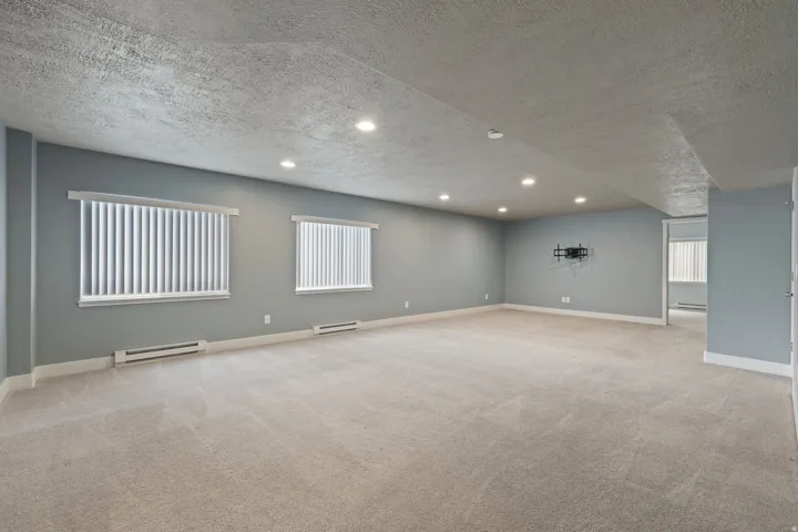 Expansive room with neutral carpeting, recessed ceiling lighting, and multiple windows with vertical blinds
