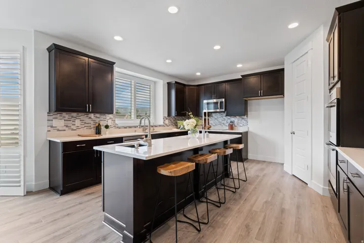 Kitchen featuring dark wood-finish cabinetry, light-toned countertops, a center island with sink, stainless steel appliances, and wood-finish flooring