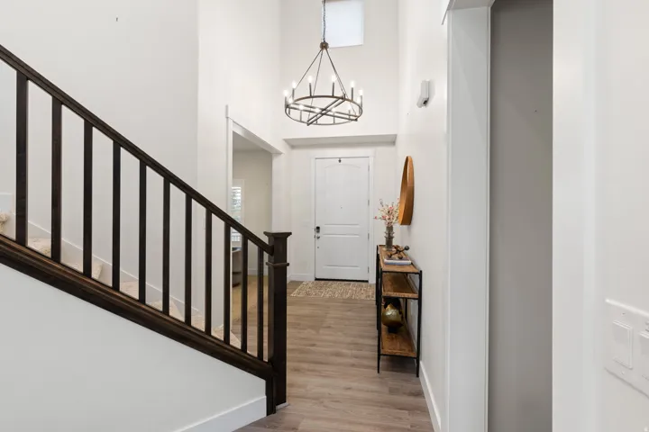 Vaulted entry with wood-finish flooring, dark wood newel post and balusters, and a black wrought iron chandelier