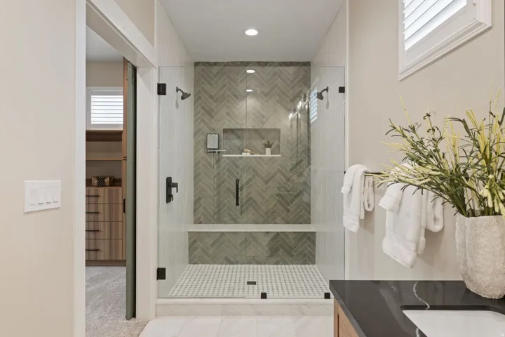 Spa-inspired primary bathroom featuring a frameless glass-enclosed shower with herringbone tile surround, linear drain, and integrated bench seating