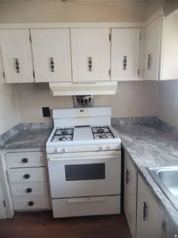 White cabinetry with decorative hardware, gas range, range hood, and stainless steel sink