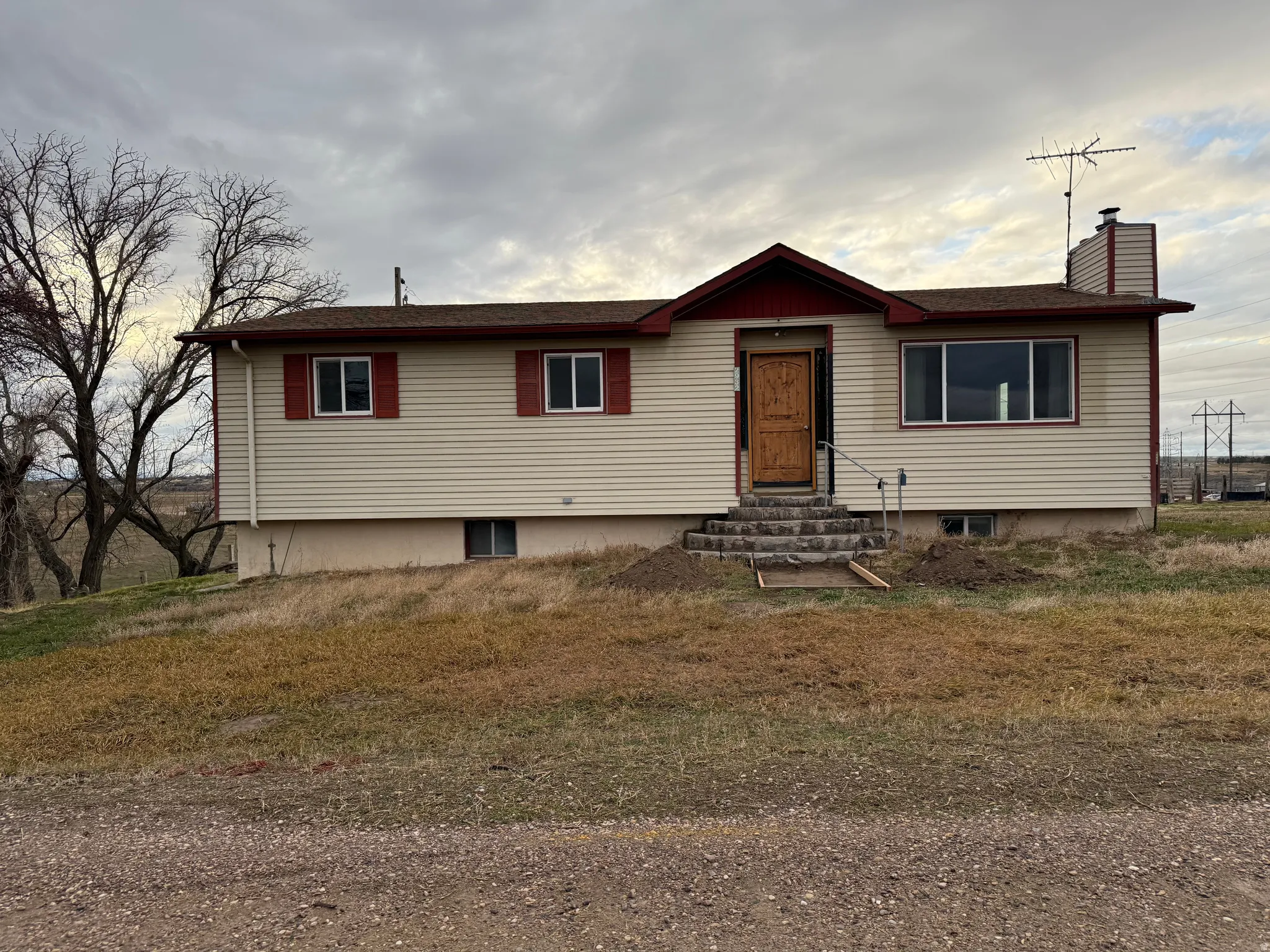 Split-level residence featuring light-colored siding, a brown shingle roof, and red trim accents