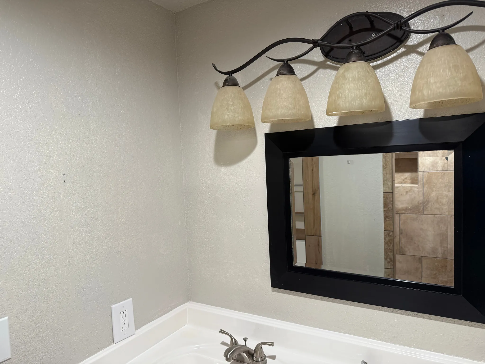 Four-light vanity fixture with frosted glass shades, a wall-mounted mirror with a black frame, and a white countertop with a two-handle faucet