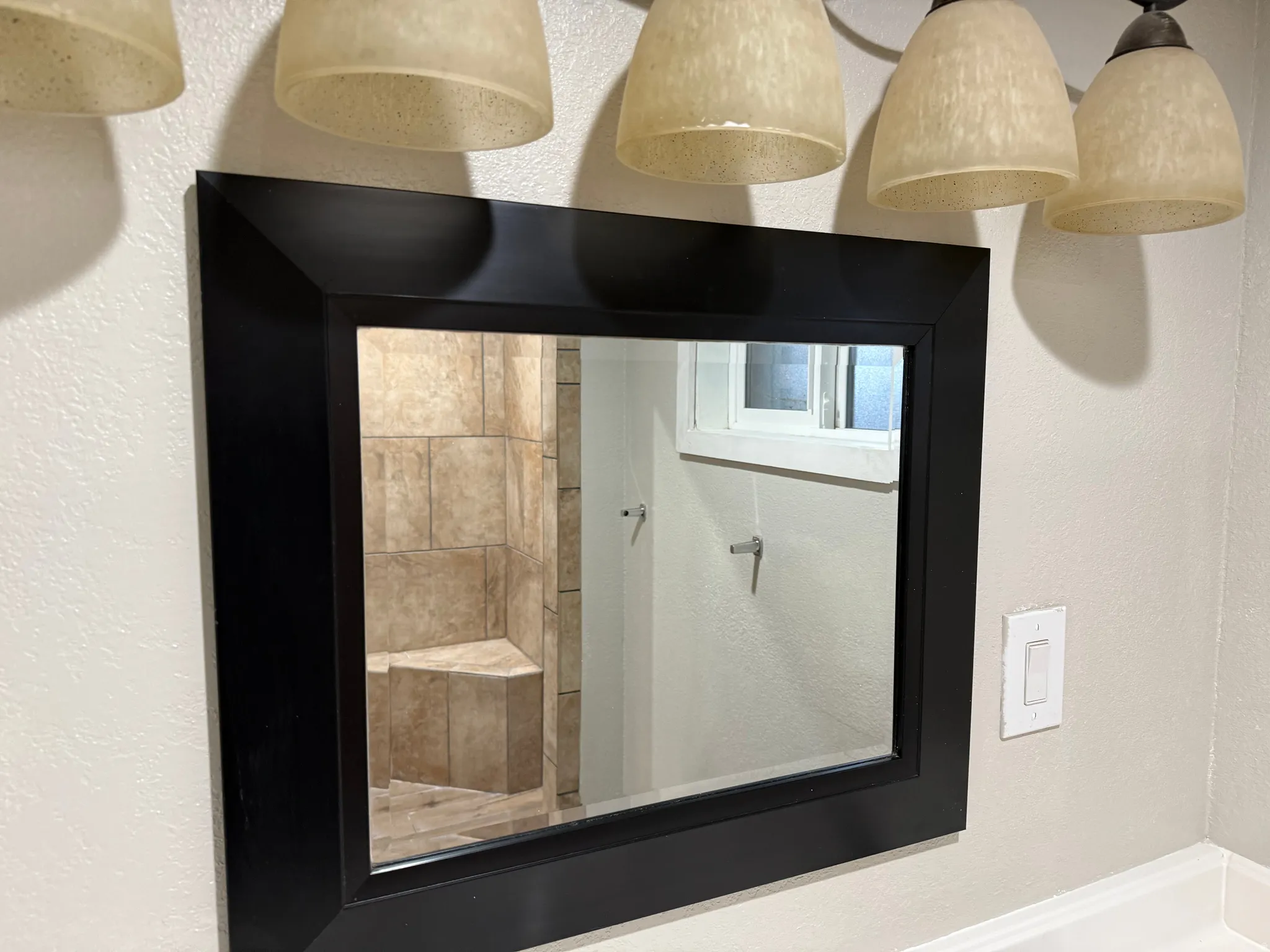 Black-framed mirror with an overhead three-light fixture