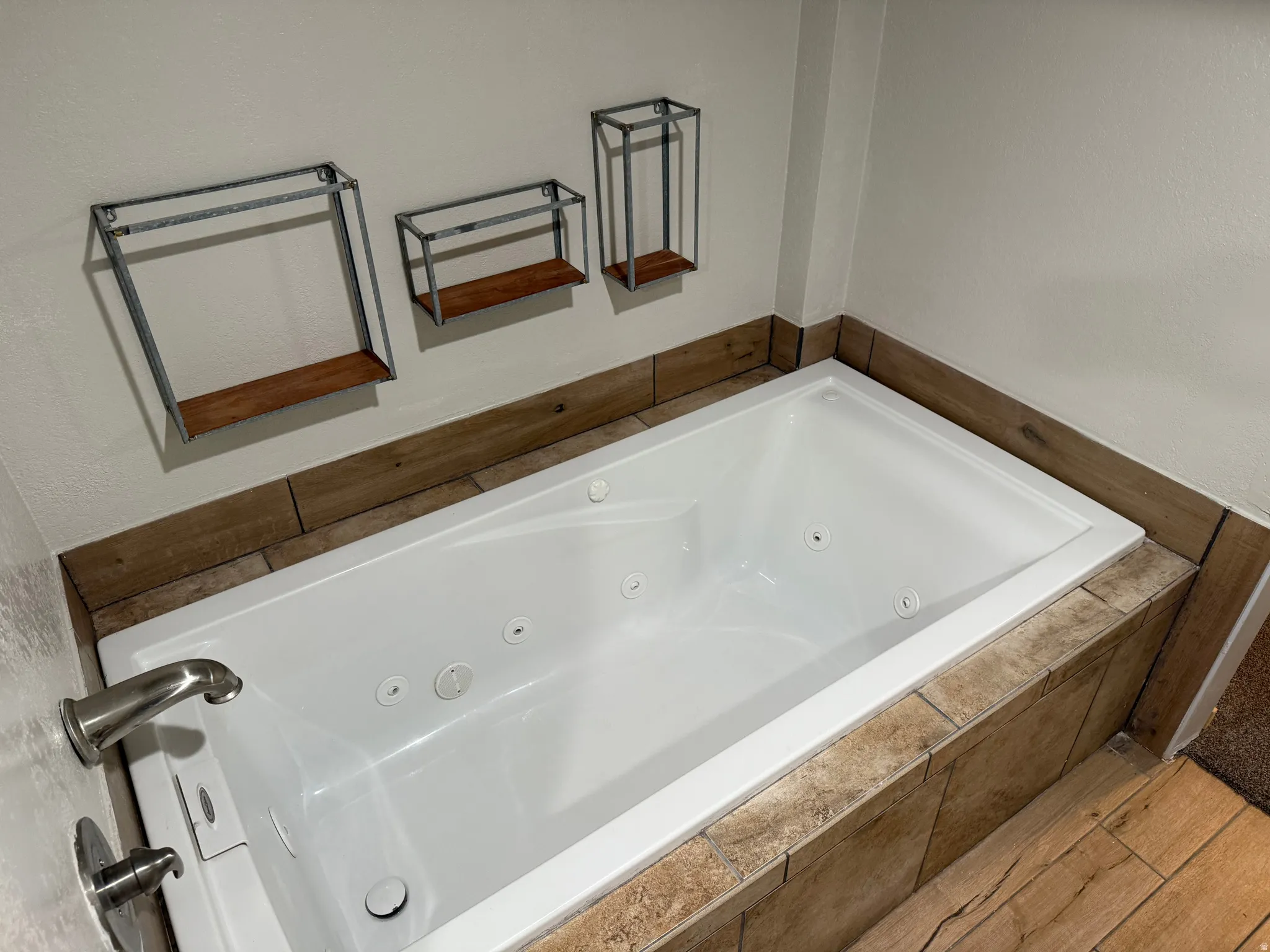Jetted soaking tub with brushed nickel fixtures, surrounded by wood-finish tile and wall-mounted shelving