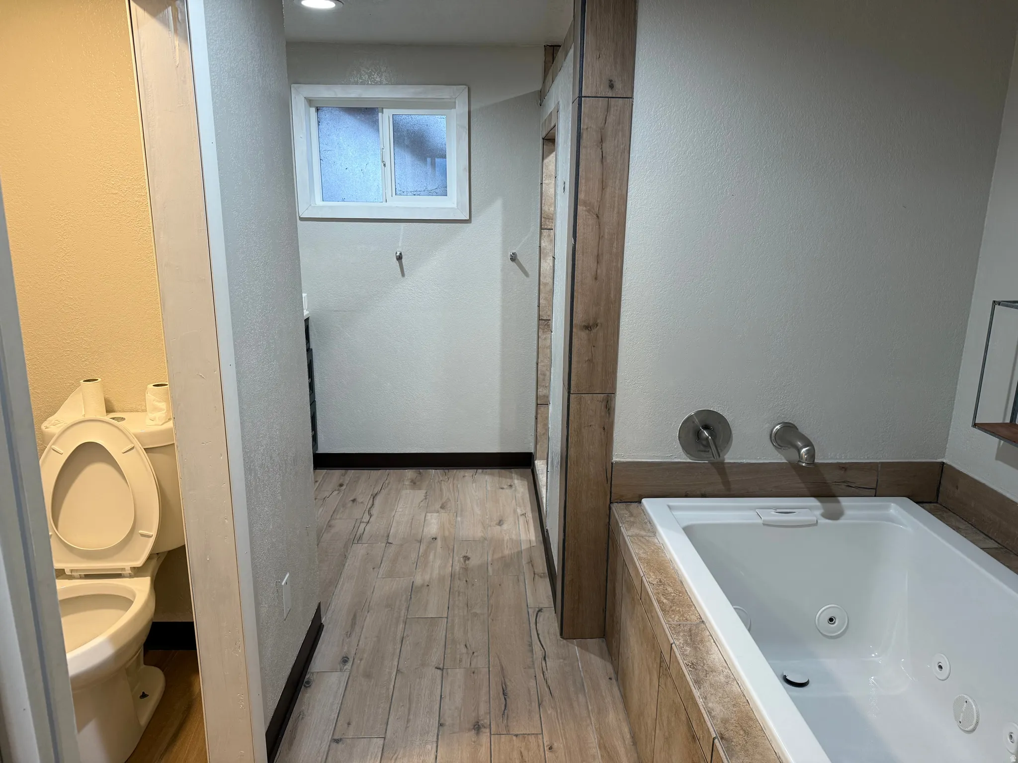Soaking tub with integrated jets, wood-finish tile surround, and wall-mounted fixtures