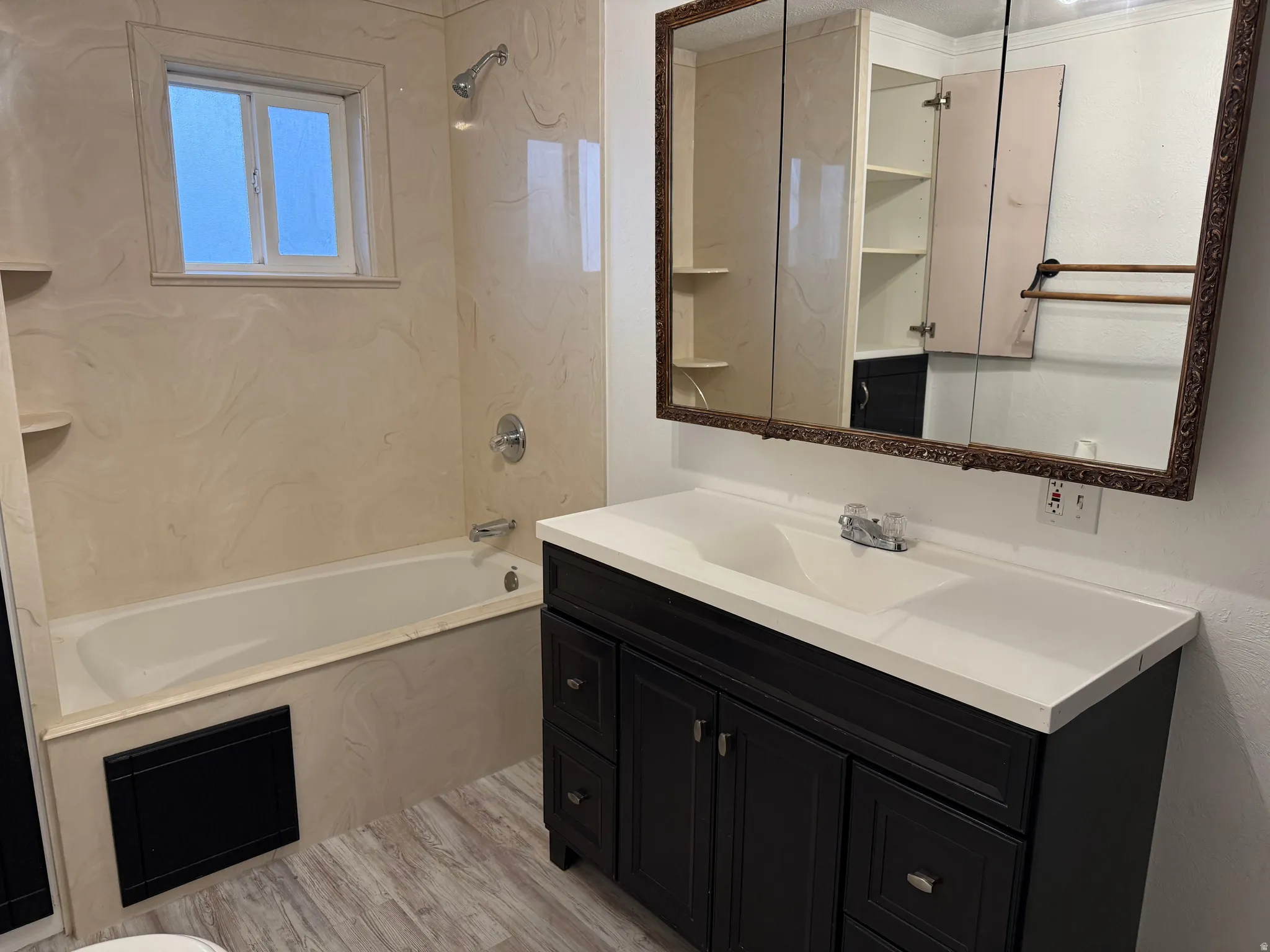 Bathroom featuring a single vanity with a white countertop and dark wood-finish cabinetry, built-in bathtub with light-toned wall surround, and wood-finish flooring