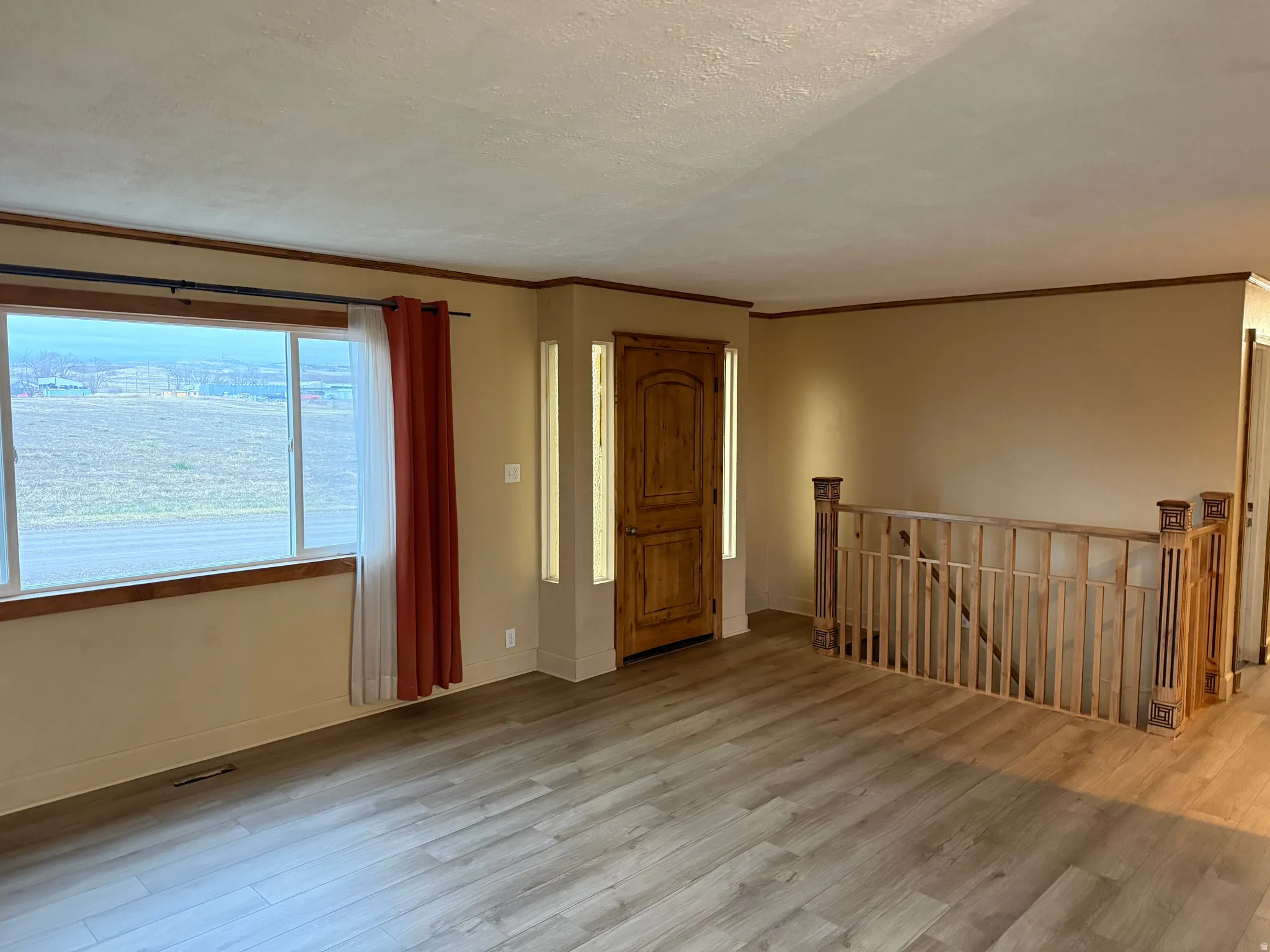 Expansive window, wood-finish flooring, staircase with wood railing, warm wall tones, and crown molding