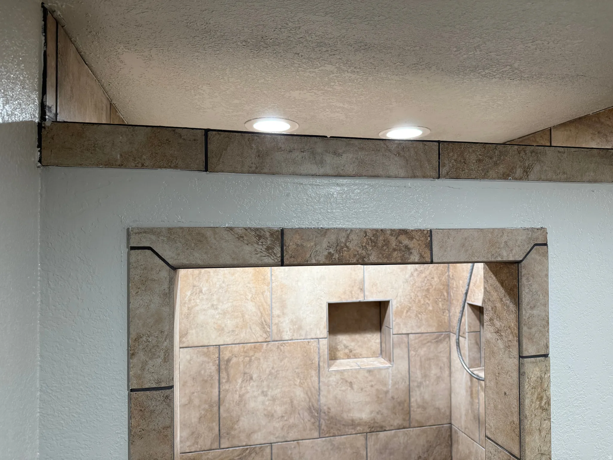 Recessed lighting illuminating a tiled shower enclosure featuring a built-in niche