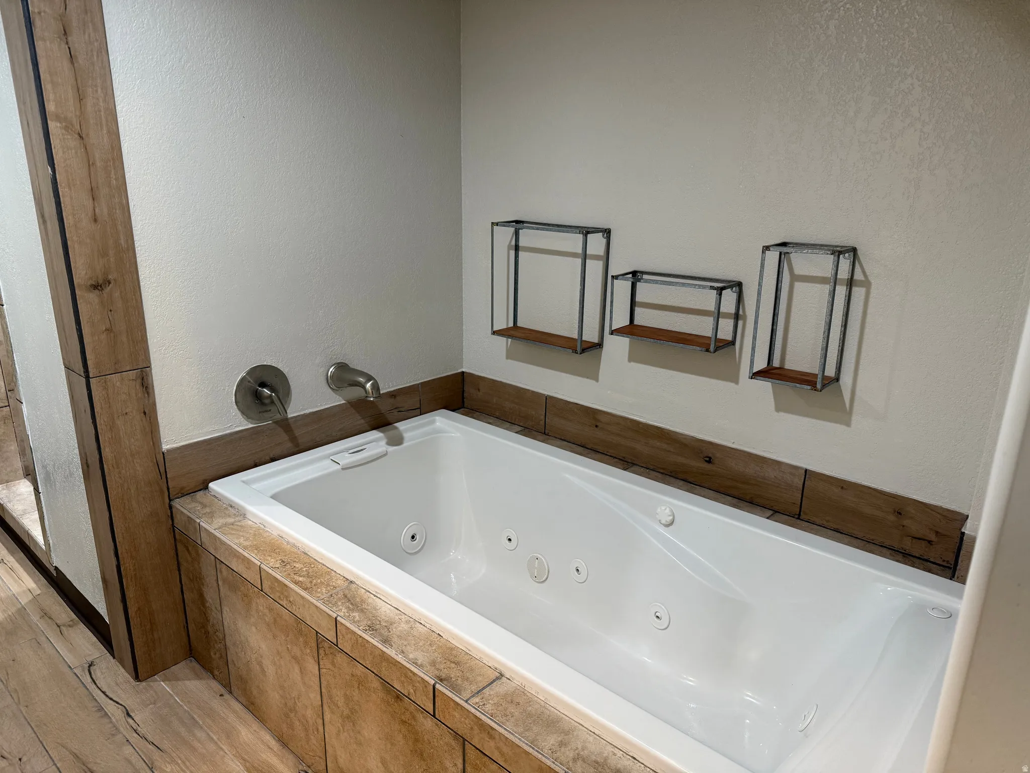 White soaking tub with jetted features, brushed nickel fixtures, and wood-finish tile surround