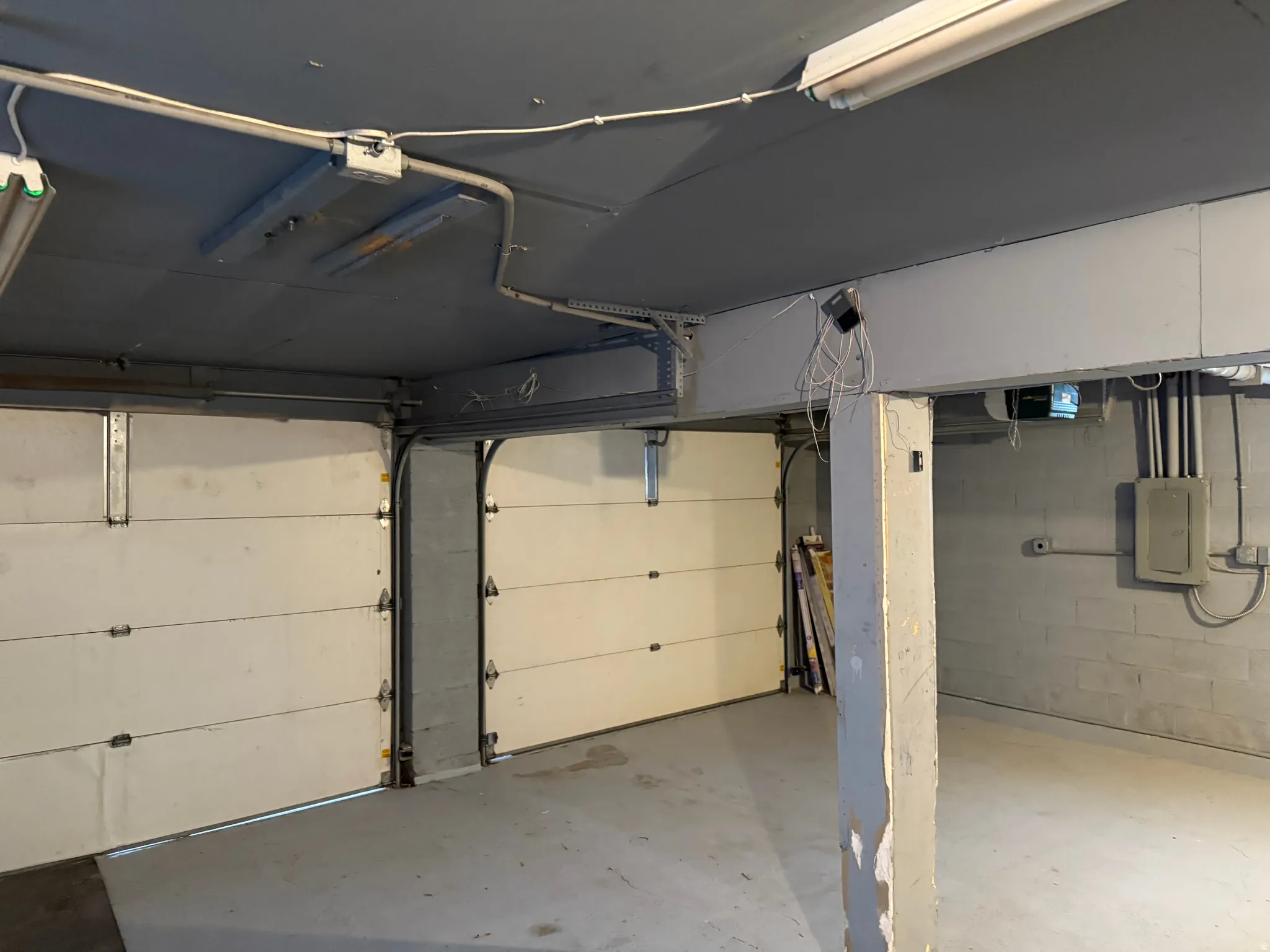 Two garage doors, painted concrete flooring, exposed ceiling conduit, and a concrete block wall