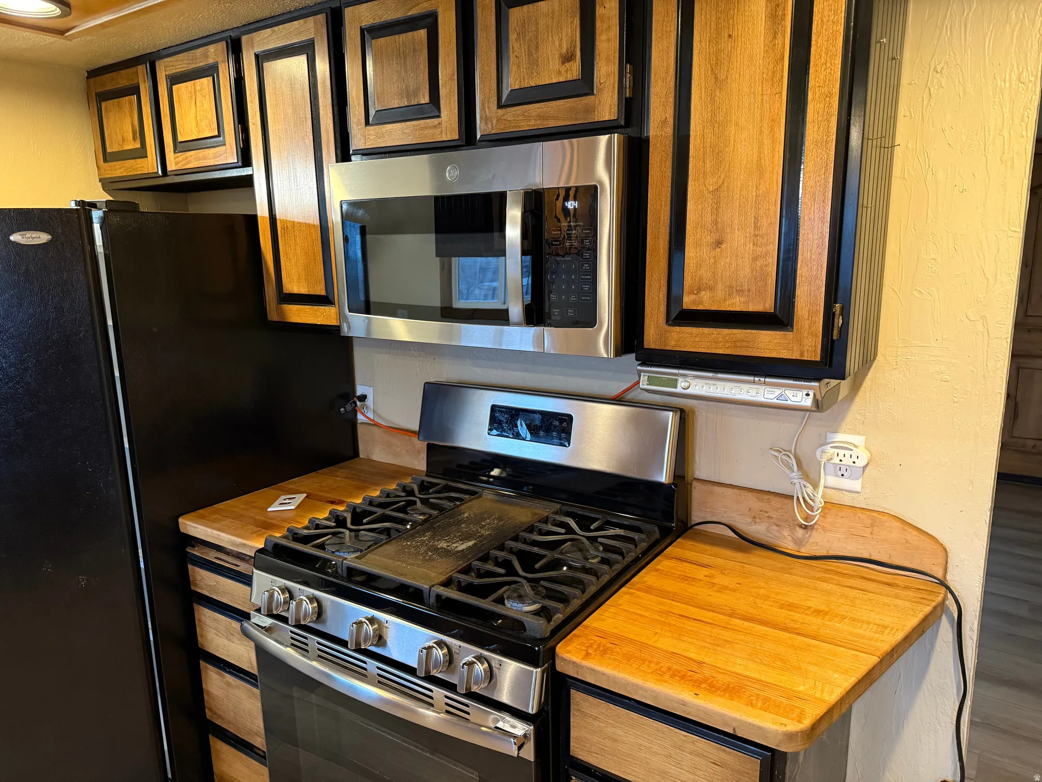 Stainless steel microwave, gas range, wood-finish countertops, wood-finish cabinetry, and black refrigerator