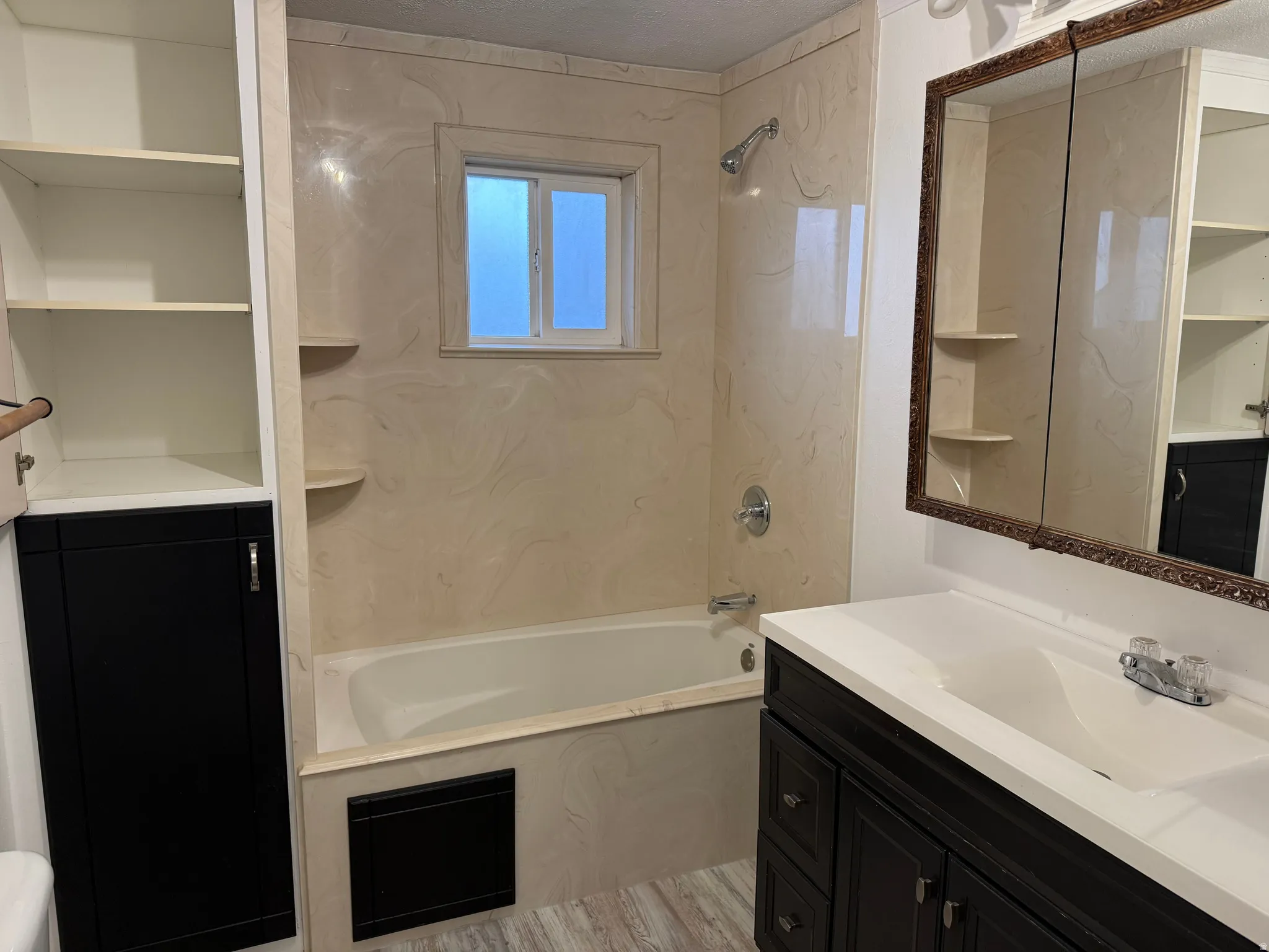 Built-in shelving, integrated bathtub with shower, dark wood-finish vanity with white countertop, framed medicine cabinet, and wood-finish flooring