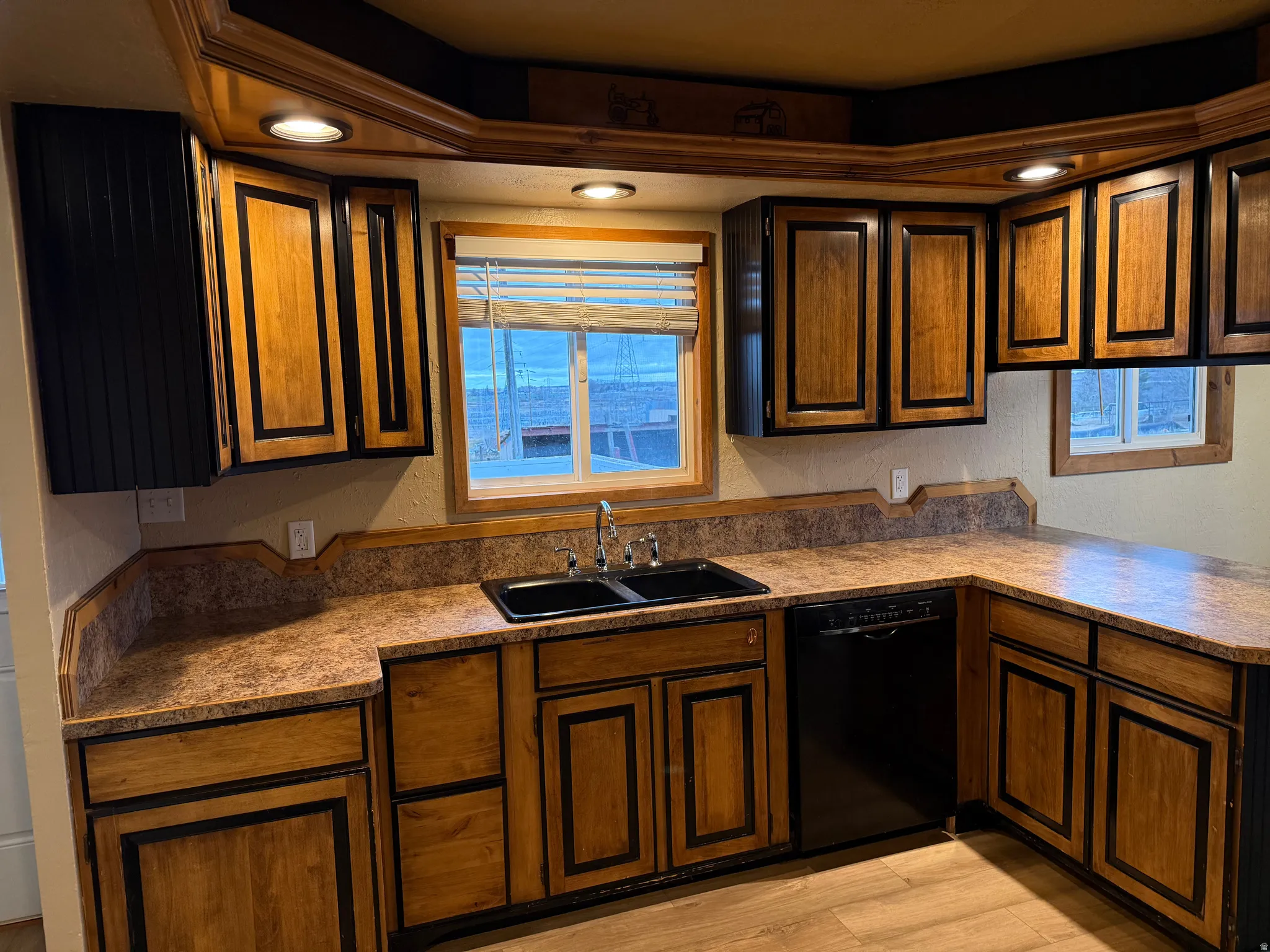 U-shaped kitchen featuring wood-paneled cabinetry with dark trim, laminate countertops, a black double-basin sink, and black built-in dishwasher