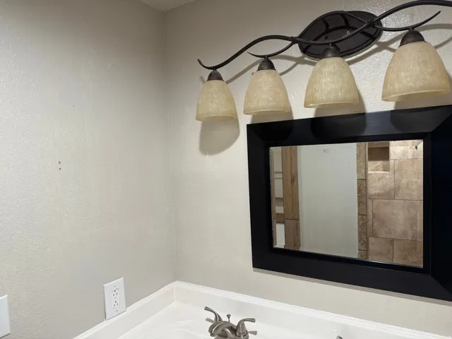 Four-light vanity fixture with frosted glass shades, a wall-mounted mirror with a black frame, and a white countertop with a two-handle faucet