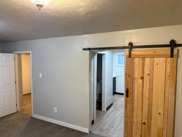 Rustic wood barn door with black hardware, leading to a space with wood-finish flooring