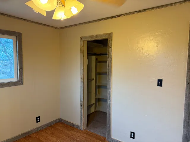 Wood-finish flooring, built-in shelving, wood-trimmed window, wood-trimmed doorway, and a ceiling fan