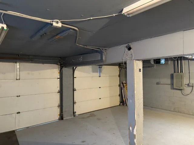 Two garage doors, painted concrete flooring, exposed ceiling conduit, and a concrete block wall