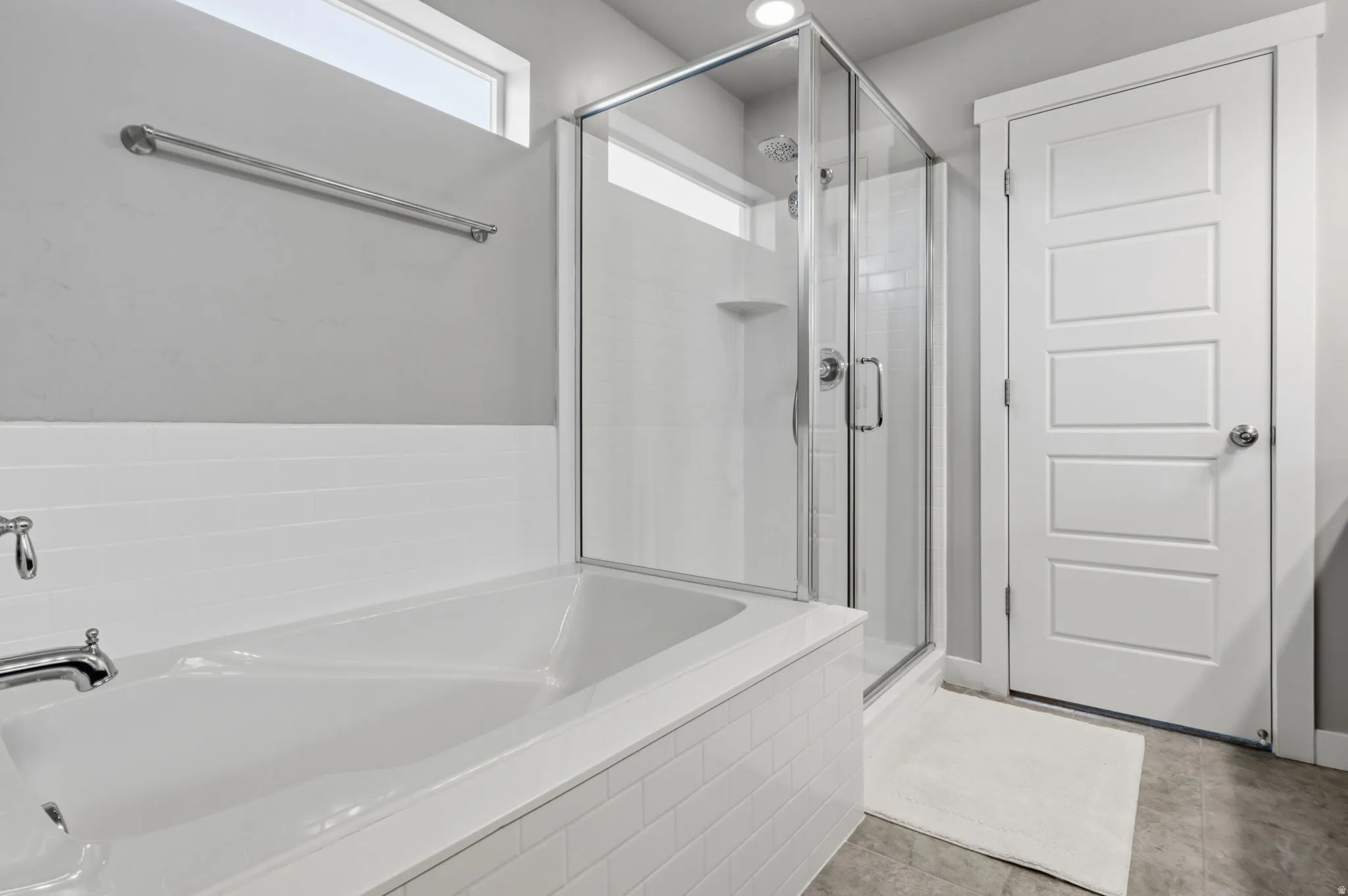 Soaking tub with white subway tile surround, glass-enclosed shower, transom window, and modern panel door