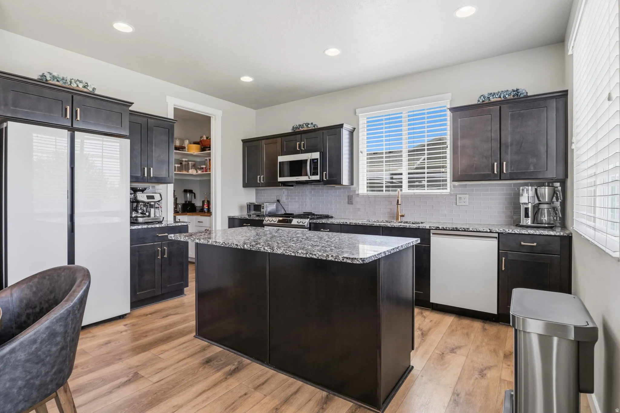 Kitchen featuring dark wood cabinetry, granite countertops, a tiled backsplash, stainless steel appliances, and wood-finish flooring