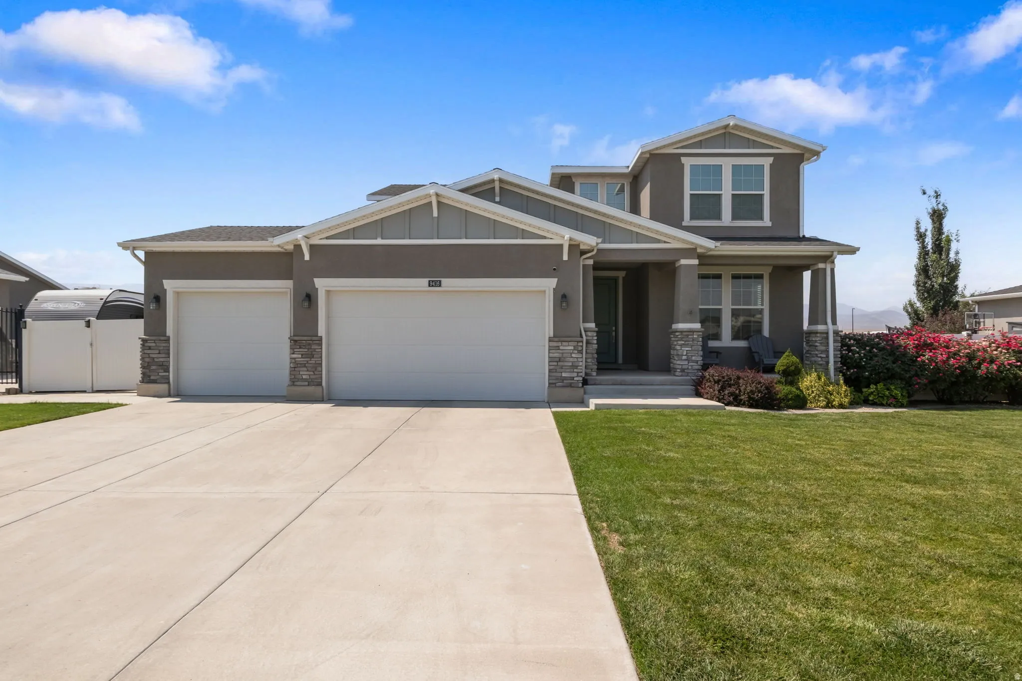 Two-story residence featuring a two-car garage, stone facade accents, covered entry, and a manicured front lawn