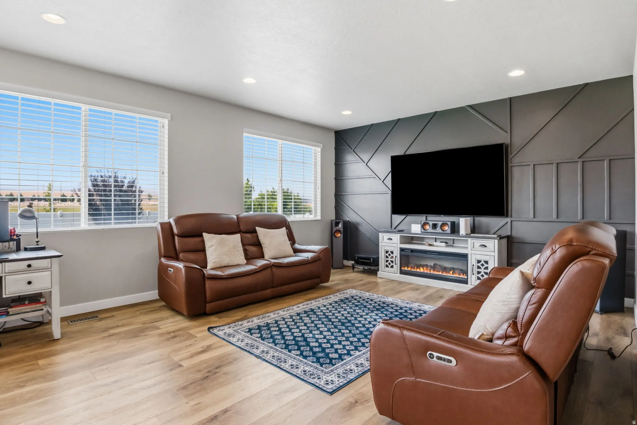 Expansive room featuring wood-finish flooring, two large windows, recessed lighting, and a decorative accent wall with an integrated electric fireplace