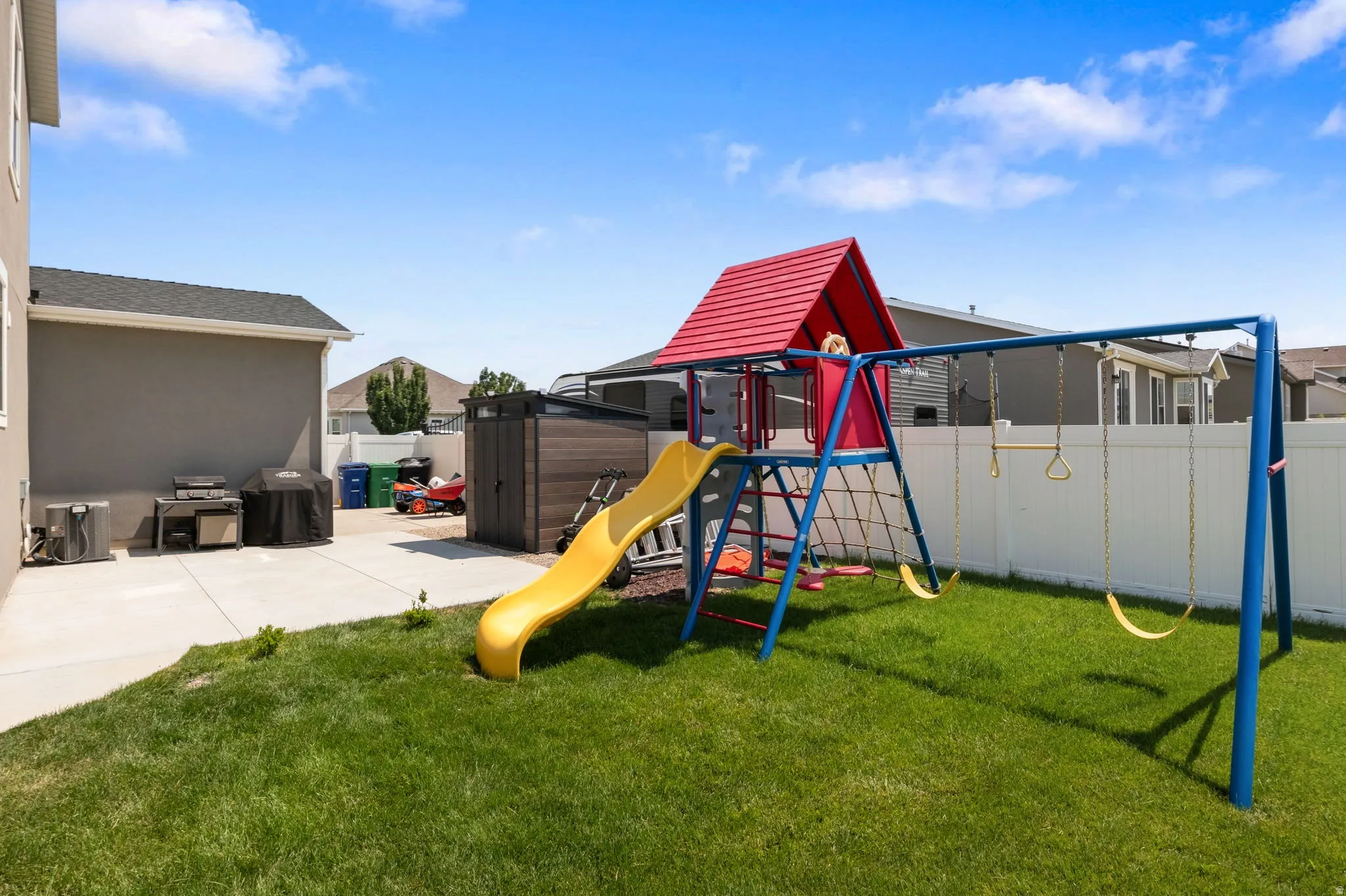 Expansive backyard featuring a lush lawn, white privacy fencing, and a concrete patio