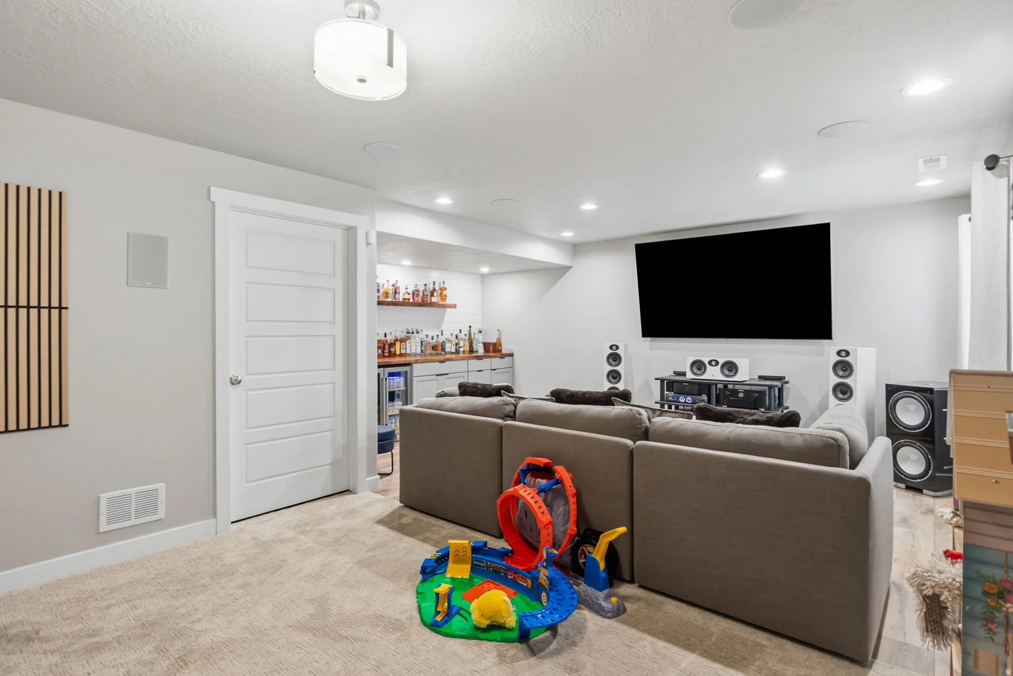 Recessed lighting illuminates this space, featuring a built-in wet bar with open shelving, wood-finish flooring, and a ceiling-mounted light fixture