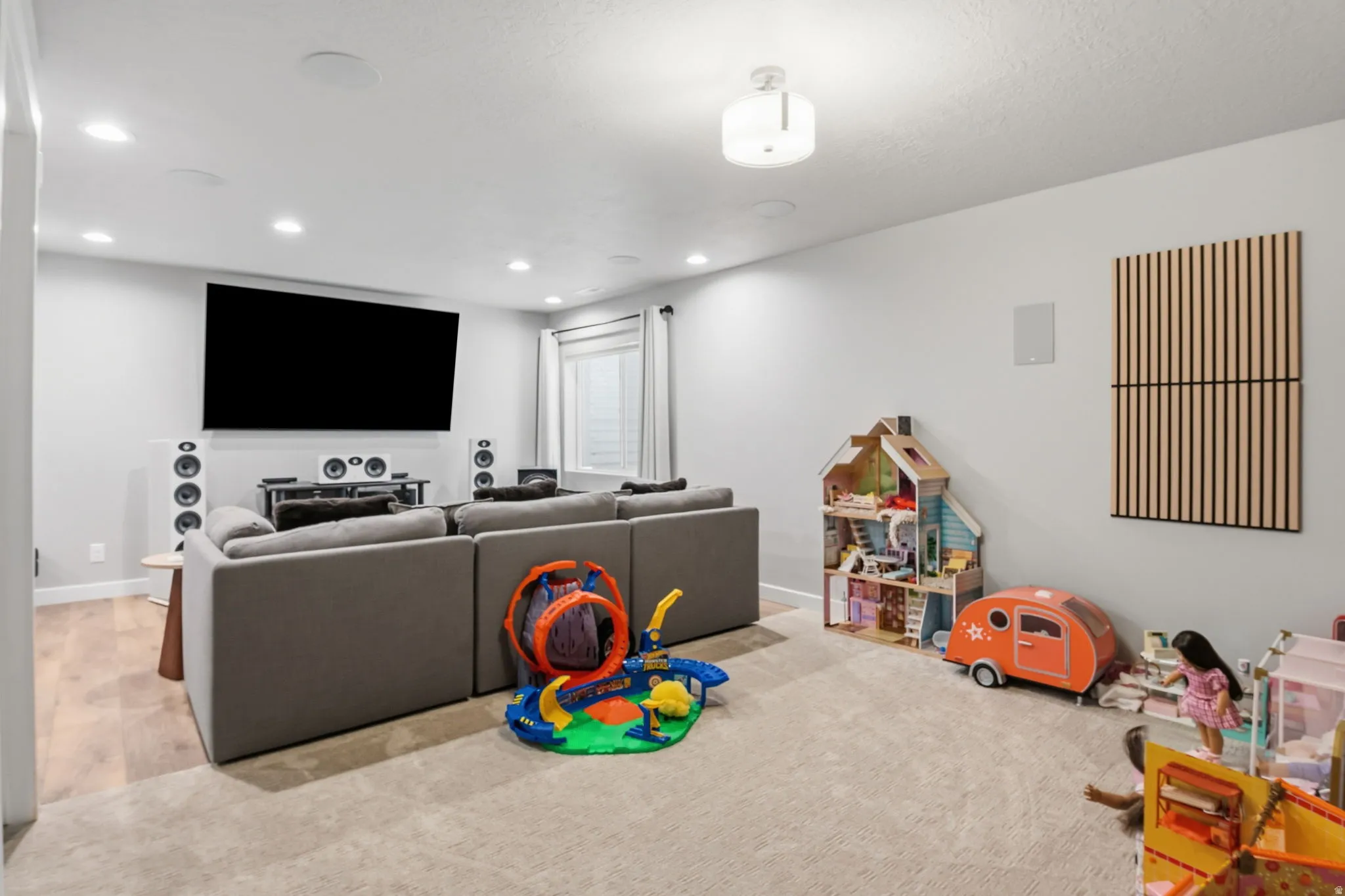 Recessed ceiling lighting, large screen display, light wood-finish flooring, and a window with blinds