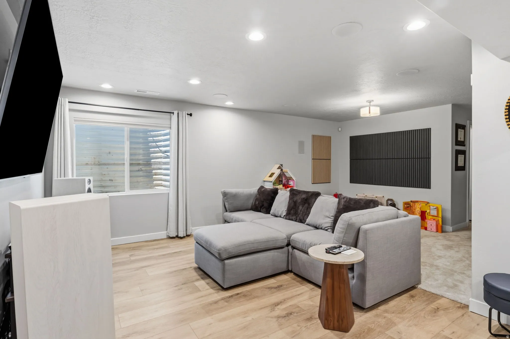 Recessed lighting illuminates wood-finish flooring, complemented by a large window with white blinds and curtains