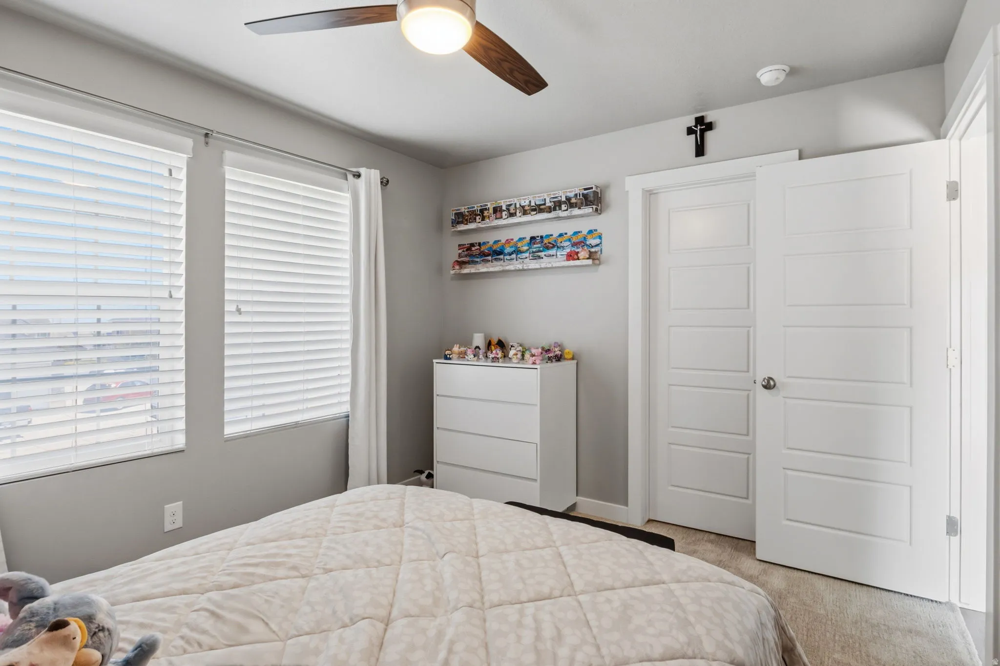 Light gray wall finishes with white trim, two white-paneled doors, dual windows with blinds, and a ceiling fan with integrated lighting